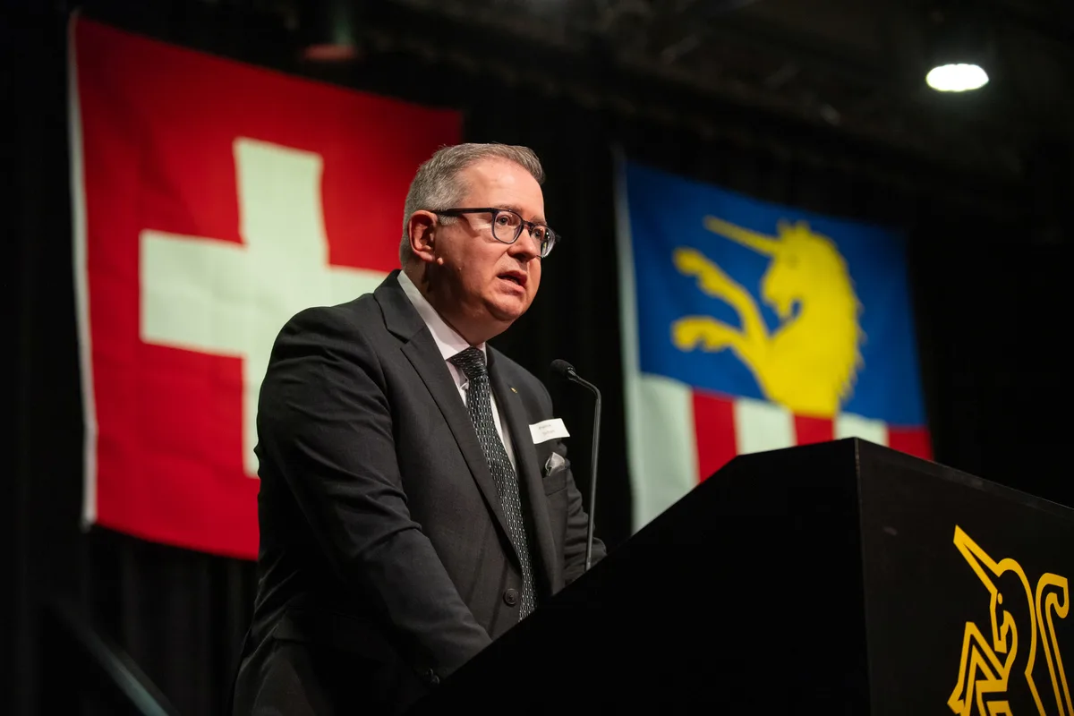 Ein Mann in einem Anzug steht an einem Rednerpult und spricht. 